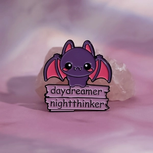 Macro shot of purple bat enamel pin with daydreamer and nightthinker text banners