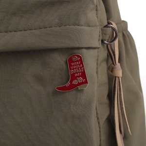 Detail of red cowboy boot enamel brooch with Dolly text on an olive canvas bag