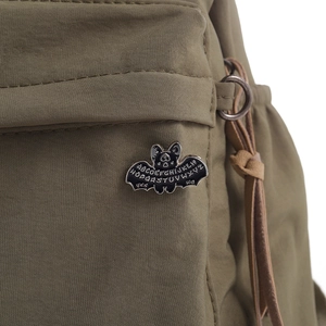 Detail of a black bat enamel pin with Ouija letters on olive green fabric bag