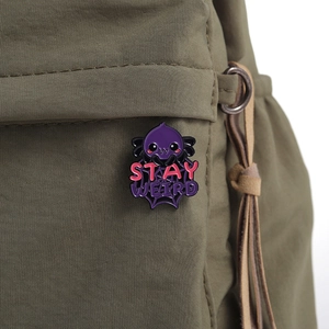 Detail of purple enamel spider pin with Stay Weird slogan on green canvas fabric