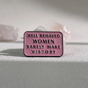 Pink enamel brooch with black text 'Well Behaved Women Rarely Make History' on pink stone