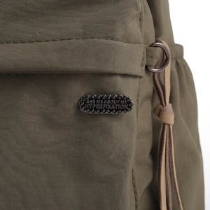 Detail of a vintage green fabric bag featuring a black metal slogan pin badge