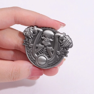Gothic punk skull metal badge with embossed bones and chain details on a grey background