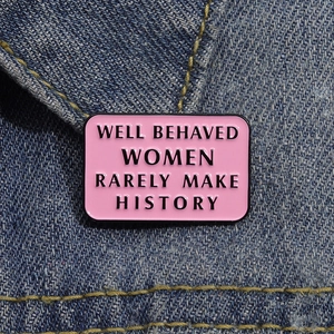 Macro shot of pink enamel brooch with black text on blue denim fabric texture