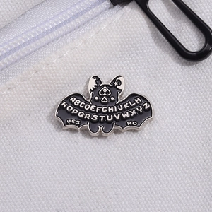 Gothic bat enamel pin with Ouija board letters on a white canvas background