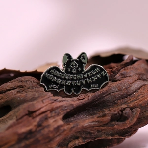 Macro detail of black bat enamel pin with gothic alphabet and ouija board engraving