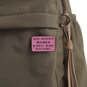 Detail of pink enamel pin with 'Well Behaved Women Rarely Make History' quote on green bag