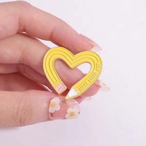 Yellow heart-shaped pencil enamel brooch with MAKE MORE ART text on denim jacket