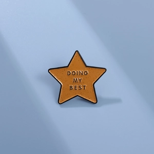 Star-shaped enamel pin badge in orange with DOING MY BEST text on light blue background
