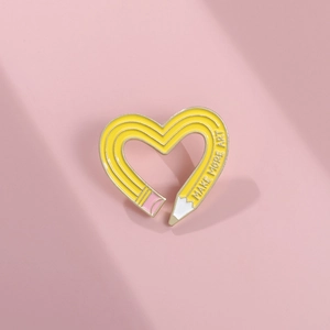 Macro detail of heart-shaped yellow enamel pencil brooch with Make More Art engraving