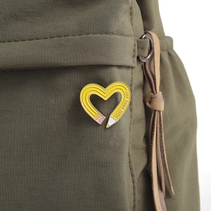 Detail of heart-shaped pencil enamel pin with Make More Art text on canvas bag