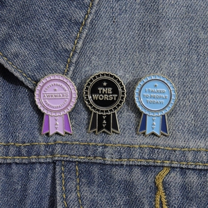 Three colorful enamel award ribbon pins with witty quotes on blue denim jacket