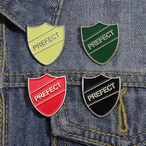 Colorful shield-shaped metal enamel brooches with PREFECT lettering on denim fabric