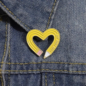 Minimalist yellow heart pencil enamel brooch with Make More Art text on denim jacket