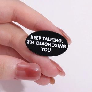 Handheld oval enamel brooch featuring black background and white KEEP TALKING funny text