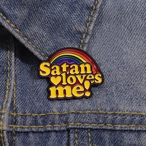 Makroansicht der Satan Loves Me Emaille-Anstecknadel mit Regenbogen auf einer Jeansjacke