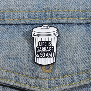 Detail of punk style trash can enamel pin with Life Is Garbage text on denim jacket