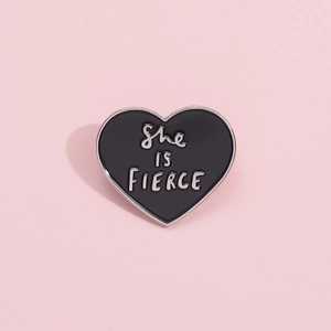 Black heart enamel brooch with 'She IS FIERCE' silver lettering on a pink background