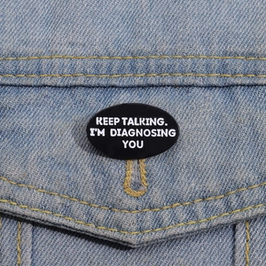 Détail d'un pin's en émail noir avec citation sur la poche d'une veste en jean