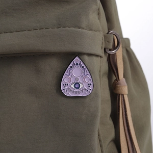 Détail d'un pin's occulte violet avec motifs lune et œil sur un sac en toile verte