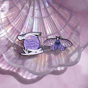 Detailed enamel pins featuring crystal ball and moth designs on iridescent tray