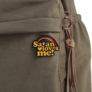 Detail einer Satan loves me Emaille-Anstecknadel mit Regenbogen auf grünem Rucksack