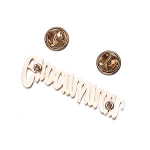 Detail of gold Empowerment letter brooch with double butterfly clutch pins on white background