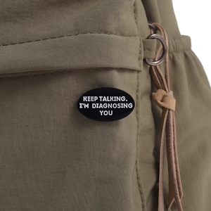 Gros plan du pin's en émail avec phrase de psychologie sur sac à dos vert armée