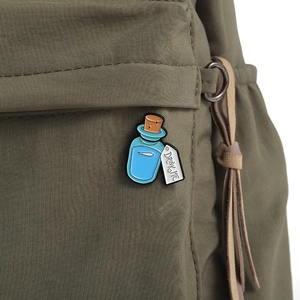 Detail of Drink Me potion enamel pin attached to an olive green nylon backpack strap