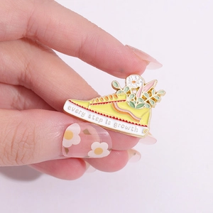 Enamel sneaker pin with white flowers and 'Every step is growth' slogan on yellow base