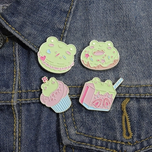 Set of four cute cartoon frog enamel pins featuring dessert and milk box designs on denim
