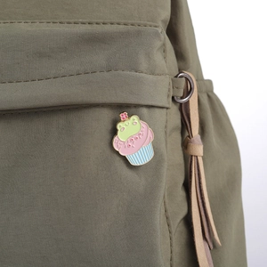 Primer plano de un pin esmaltado de rana cupcake en un bolsillo de lona verde
