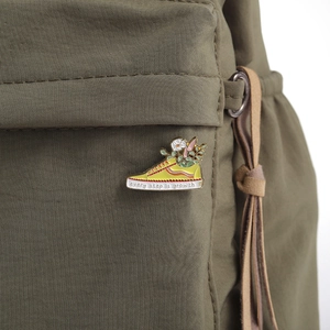 Detail of yellow canvas shoe enamel pin with flower and 'every step is growth' text