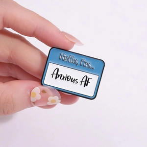 Blue and white 'Anxious AF' enamel pin badge held by hand for a backpack or jacket