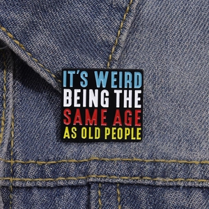 Quadratische Emaille-Brosche mit bunter Typografie an einer blauen Jeansjacke befestigt