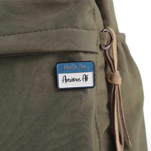 Close-up of Hello I'm Anxious AF enamel pin on a green canvas backpack strap