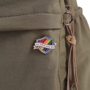 Makrodetail der Regenbogen-Schildnadel mit dem Text 'I'll Walk With You' auf grünem Stoff