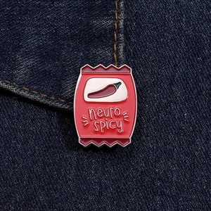 Detail of red enamel snack bag pin with neuro spicy text on dark denim fabric