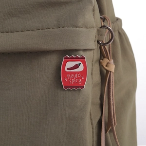 Close-up of red enamel neuro spicy snack bag brooch pinned on olive green fabric bag