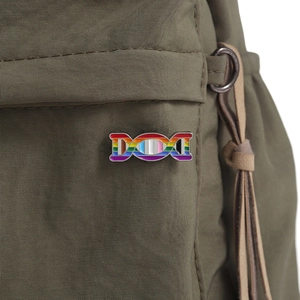 Rainbow DNA enamel pin shown on a green canvas bag as a creative science accessory