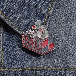 Detail of creative DJ Knight enamel pin with 'Tis But A Scratch' text on blue denim fabric