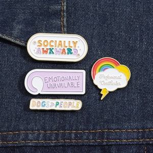 Detailed view of four colorful enamel pins with humorous slogans on denim fabric