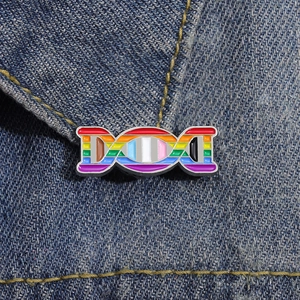 Close-up of rainbow DNA double helix enamel pin pinned on blue denim jacket fabric