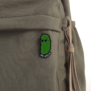 Gros plan d'un pin's humoristique en émail de cornichon sur un sac à dos vert foncé