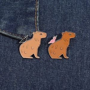 Vue macro détaillée de deux épingles en émail capybara avec oiseaux sur tissu denim