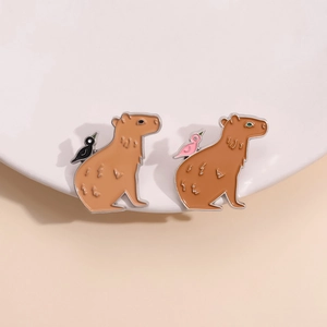 Set of two cute capybara enamel pins featuring birds on backs over white ceramic surface
