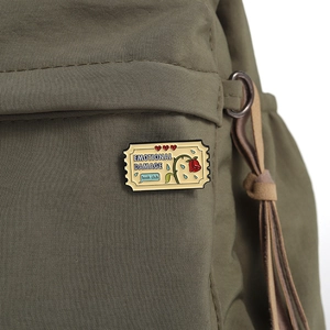 Close-up of yellow Emotional Damage enamel pin with hearts on a green backpack