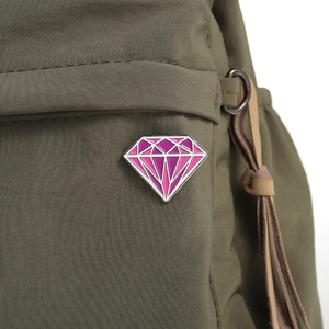 Primer plano de un broche de esmalte rosa y violeta en forma de diamante en un bolso
