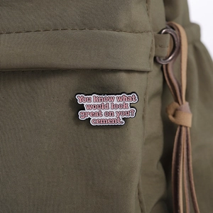Détail du badge en émail avec texte humoristique décorant un sac en tissu vert olive