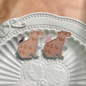 Cartoon capybara enamel pin set with bird detail on luxury gold satin and ceramic plate